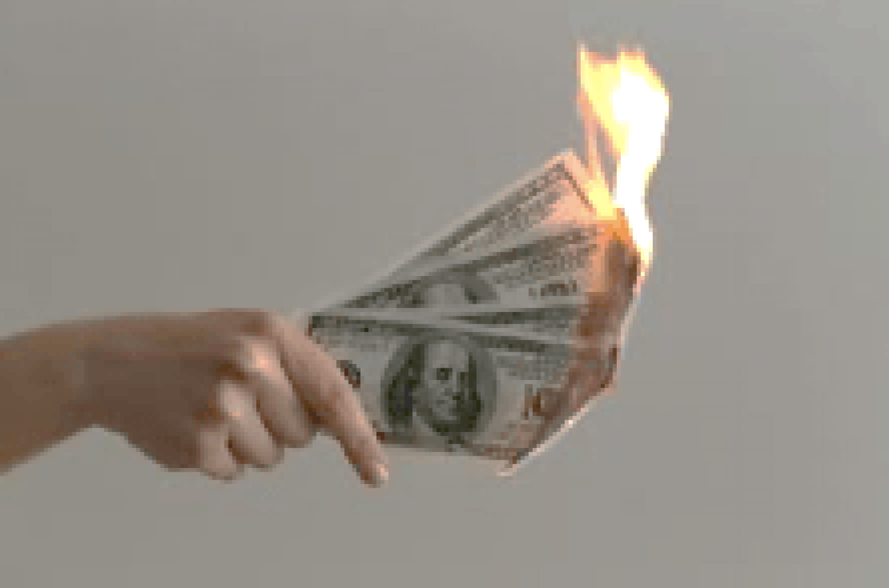 Hand holding 100 dollar bills on fire.